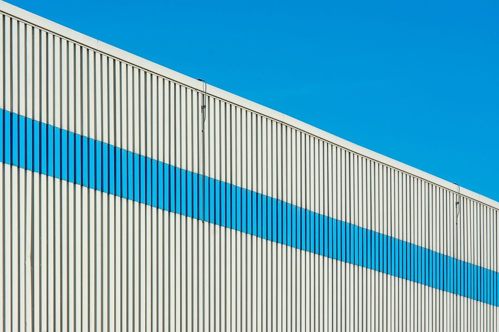 A live commercial building being re-clad bay by bay with edge protection and a cherry-picker, occupied and trading below