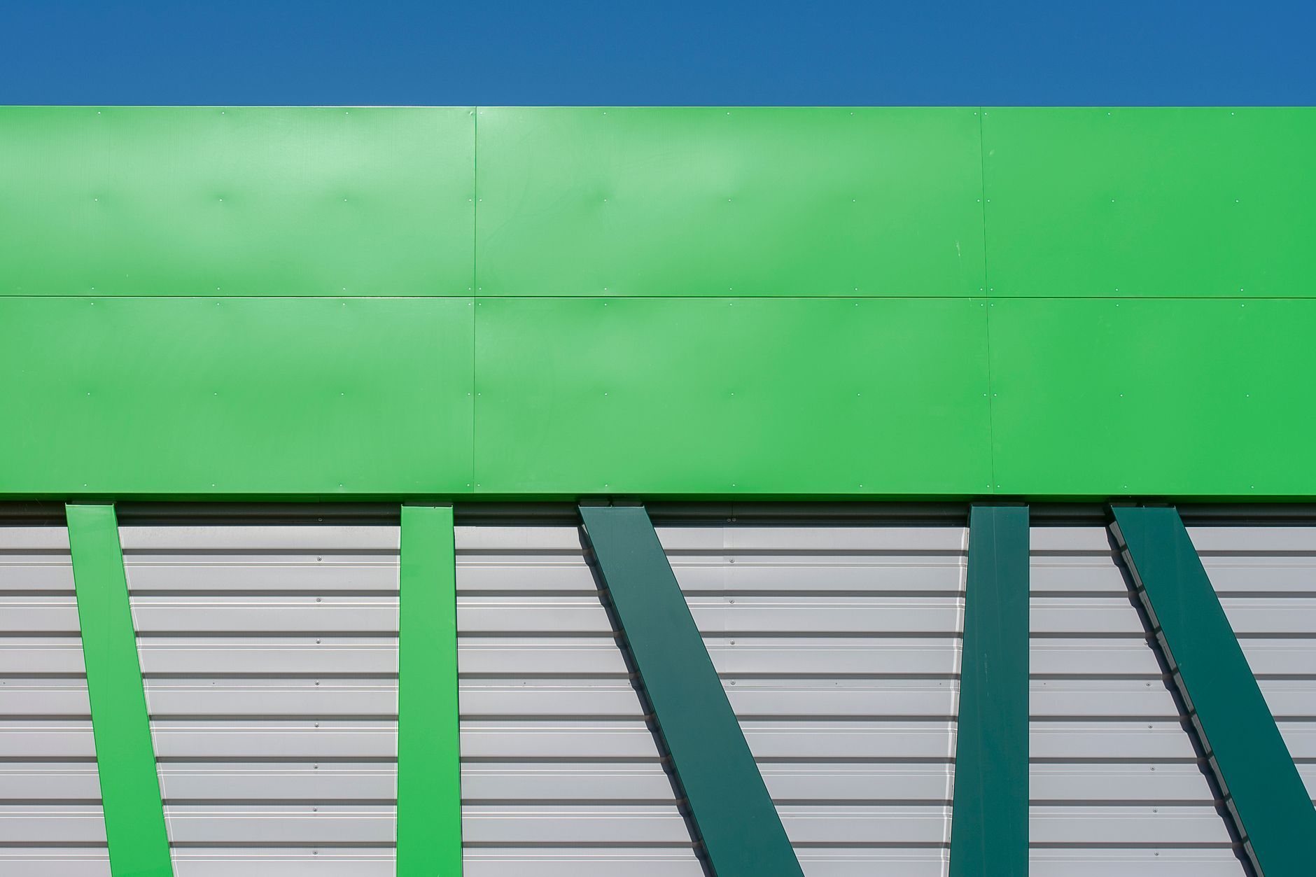 A large UK industrial roof at eaves level — profiled-metal warehouse roofing with valley gutters and rooflights under overcast daylight