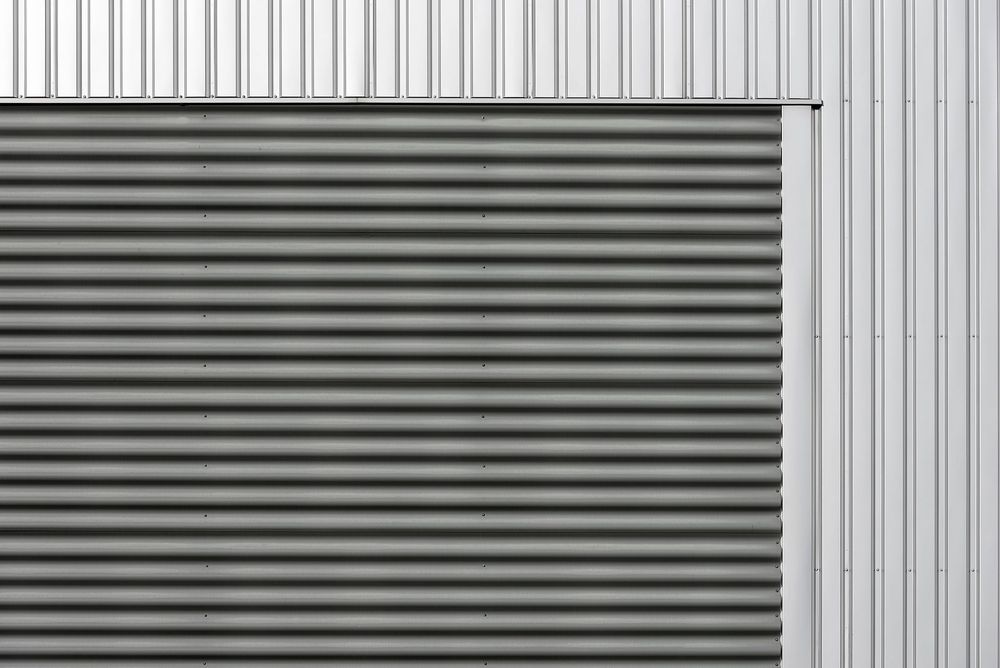 A surveyor on a commercial roof reading the build-up — checking a gutter, cut edge and cladding detail before pricing the work